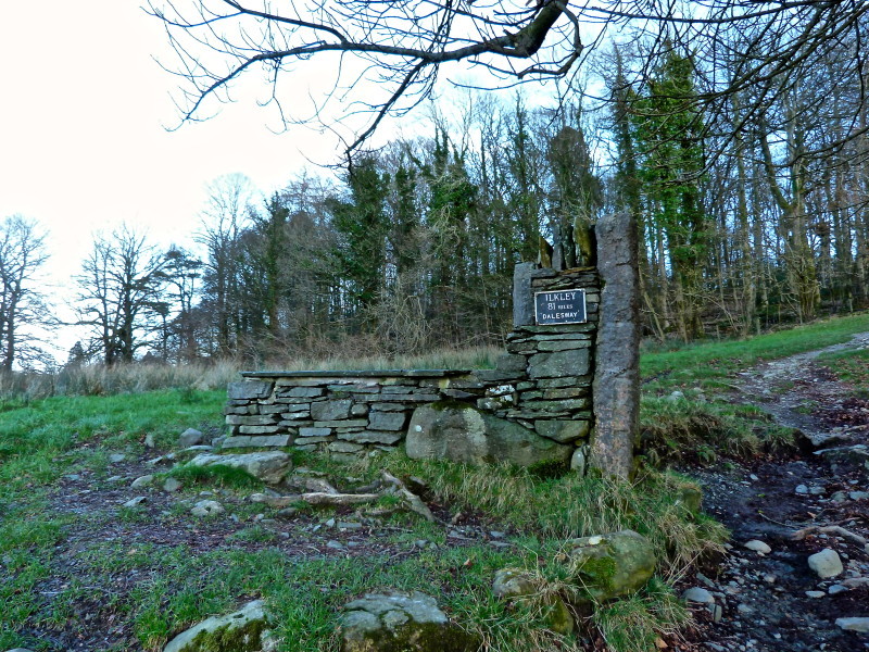 The stone seat and part wall with a plaque indicating the distance between Bowness-on-Windermere and Ilkley.